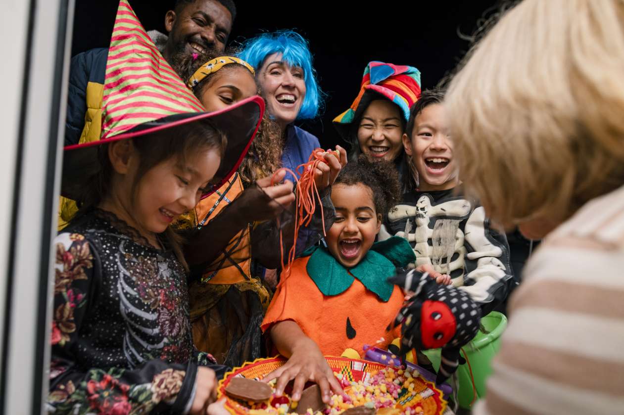A group of kids and parents help themselves to a bowl of candy while trick-or-treating.