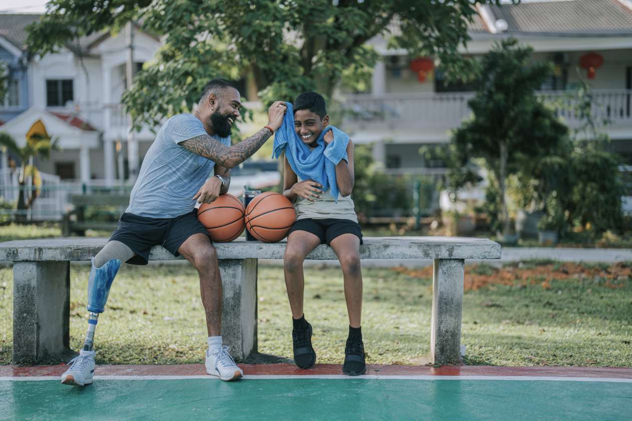 A father and his son sit on a bench, taking a break from playing basketball together.