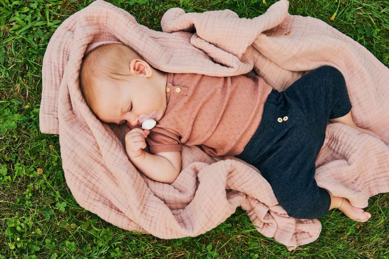 Baby naps outdoors on a blanket on grass