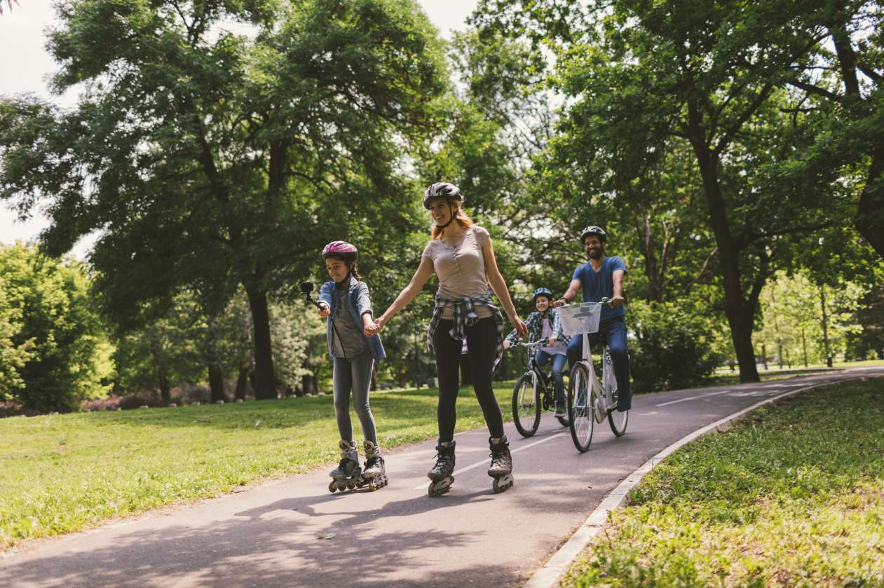 A mother and her daughter rollerblade through a park, while the father and son ride bikes behind them.