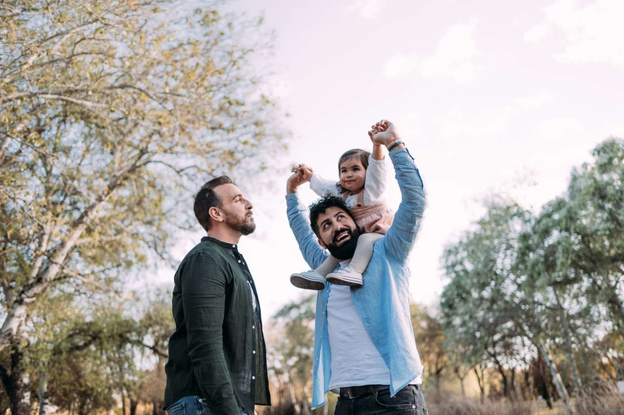Two fathers spend time outside with their toddler.