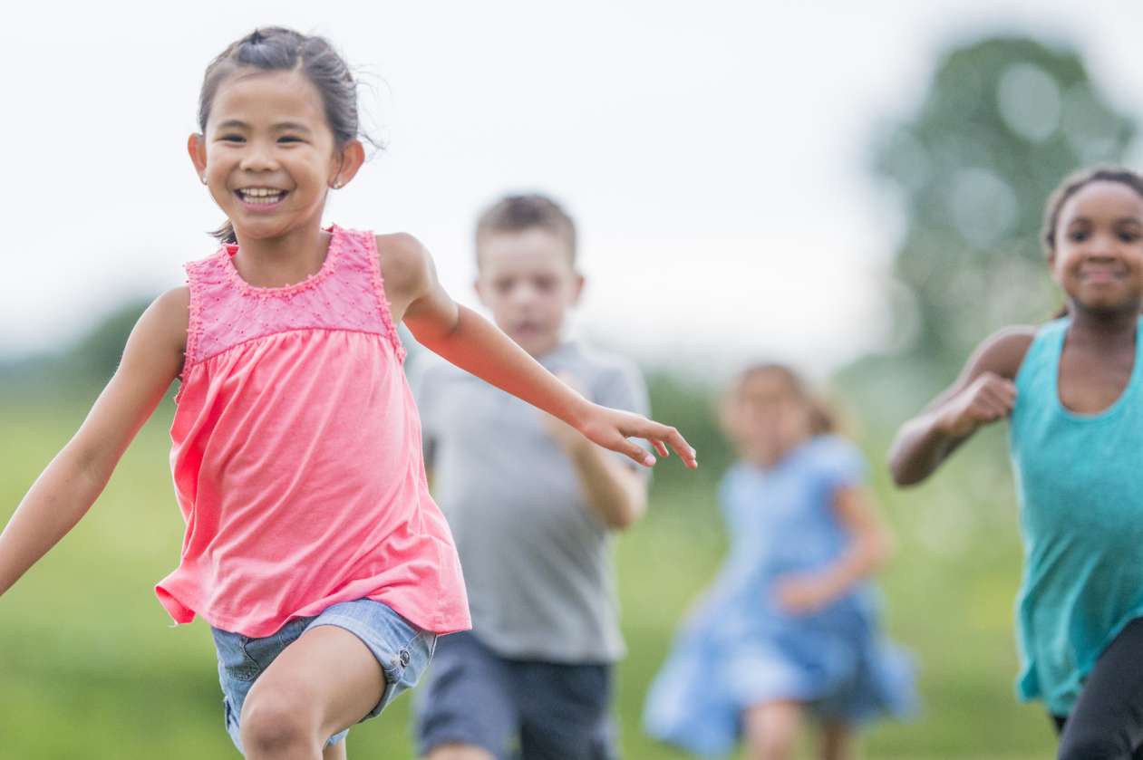 A group of elementary-age children play tag together outside during recess.