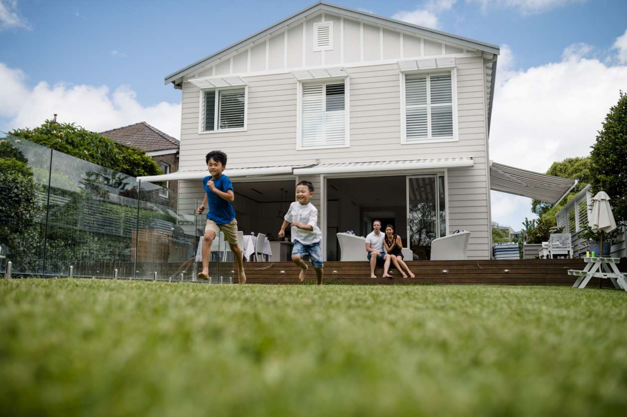Two smiling brothers race in the backyard as their parents watch from the deck.