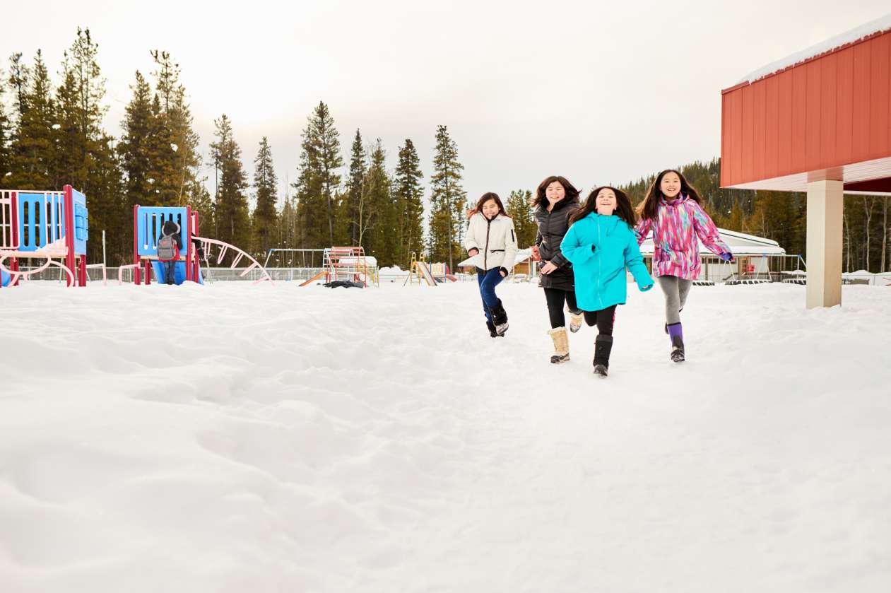 Four preteen girls run across a snowy playground at recess.