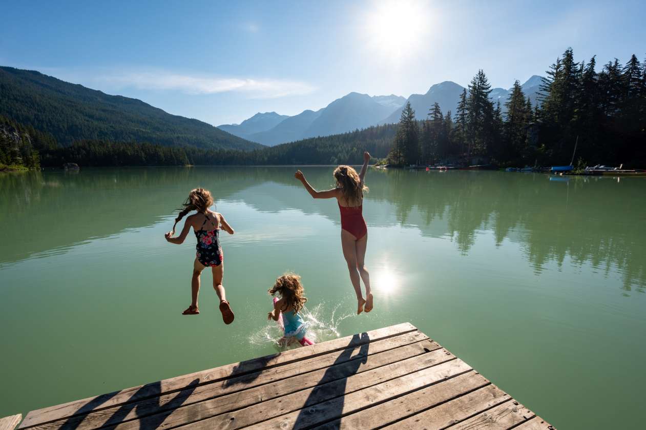 Three girls jump off a dock into a lake