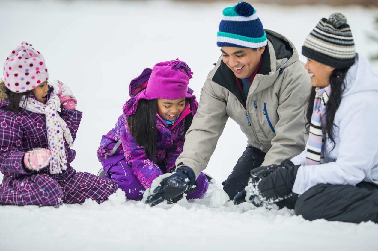 Mother, father, and two daughters playing in the snow, making snowballs
