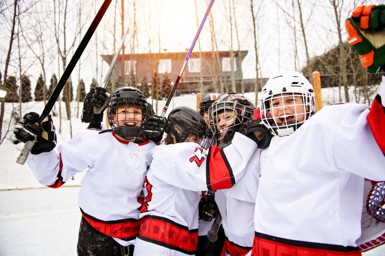 A group of kids dressed in hockey uniforms cheer as they play on an outdoor rink.