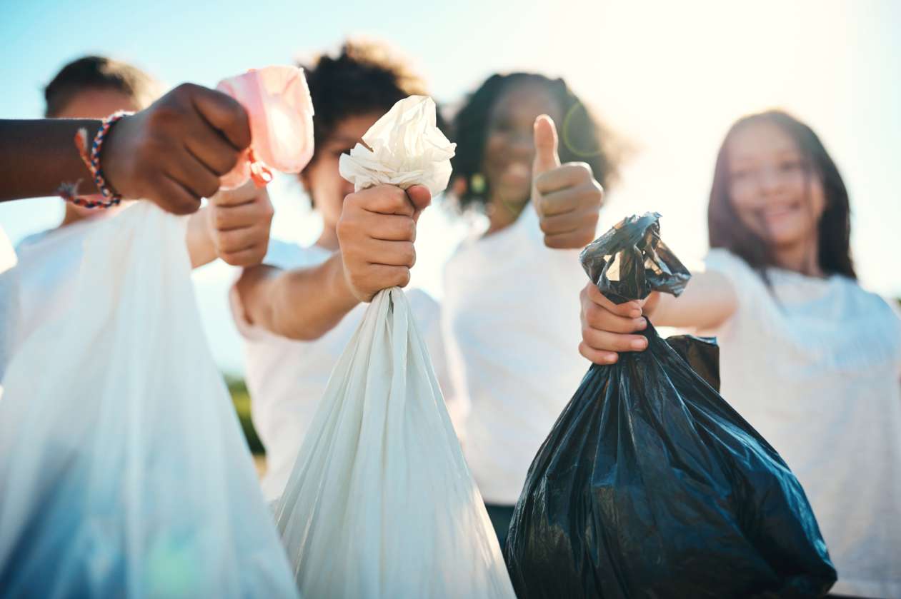 A group of kids hold up garbage bags full of litter. One girl smiles and gives a thumbs-up.