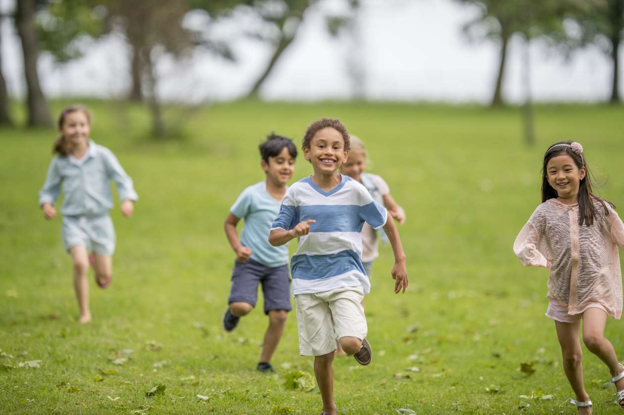 A group of elementary-age children run across a grassy field, laughing.