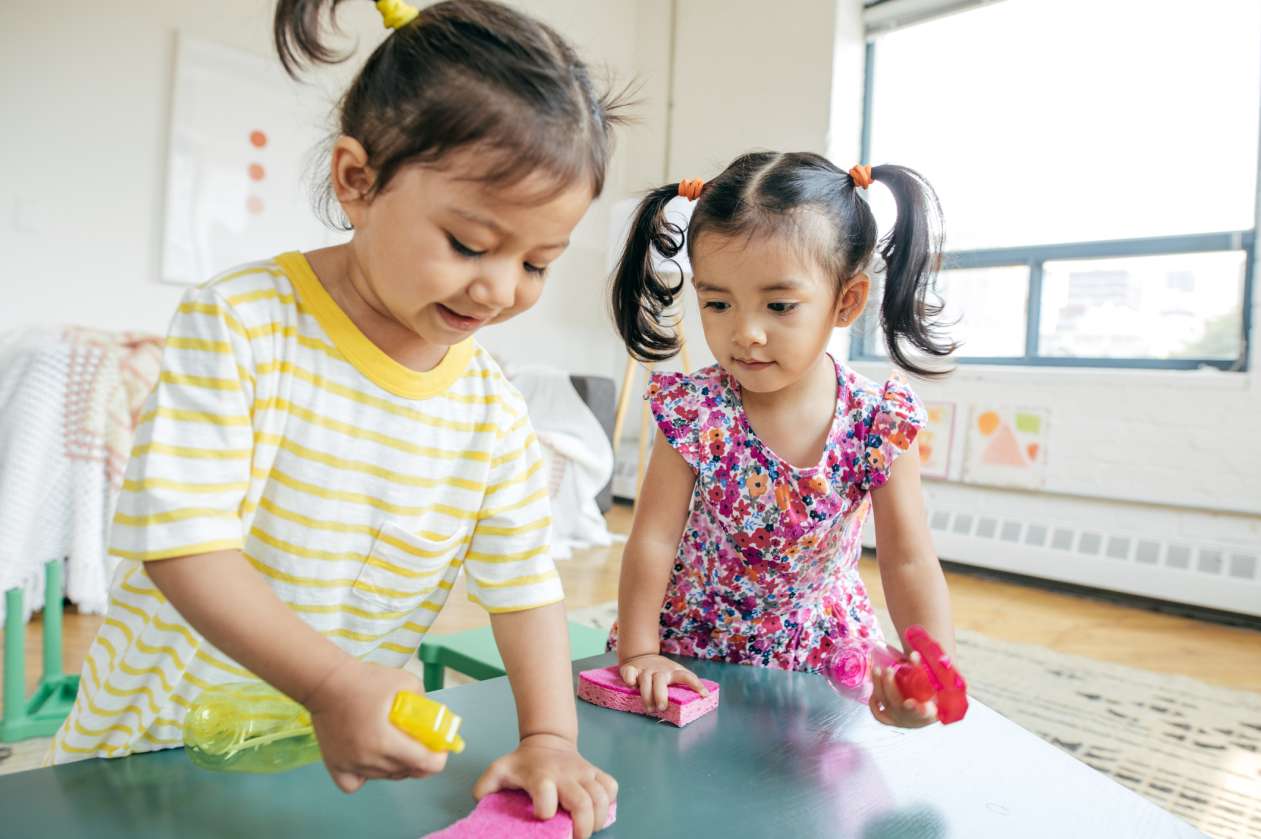 Two toddler girls stand at a table and play with toys