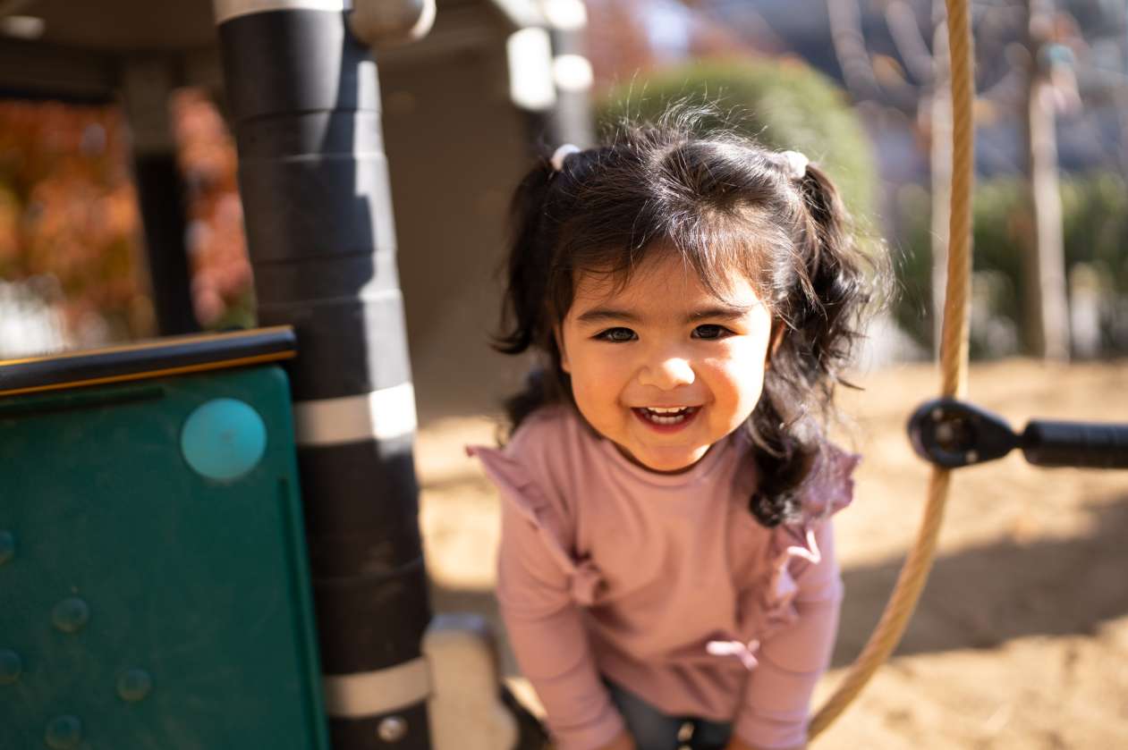 A toddler girl plays on a playground on a sunny day.