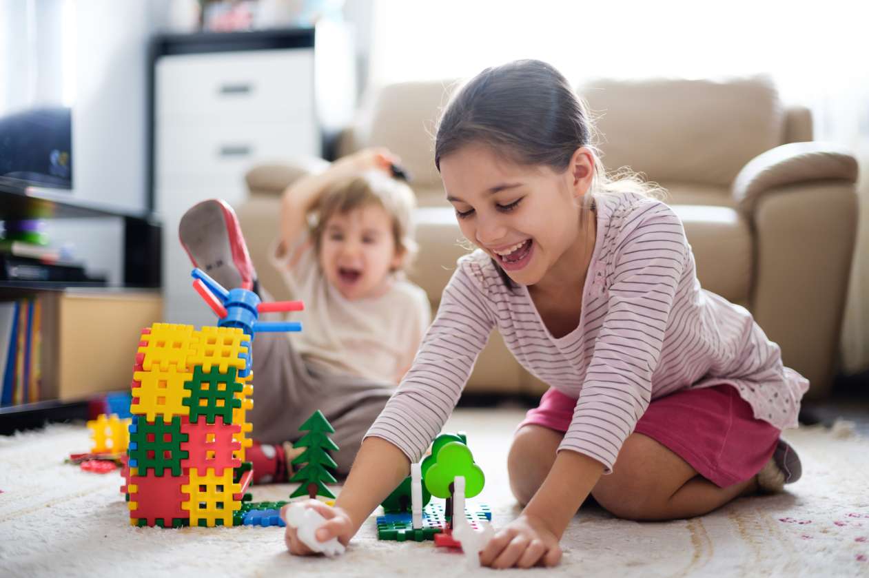 A young brother and sister play at home together with toys on the living room carpet.
