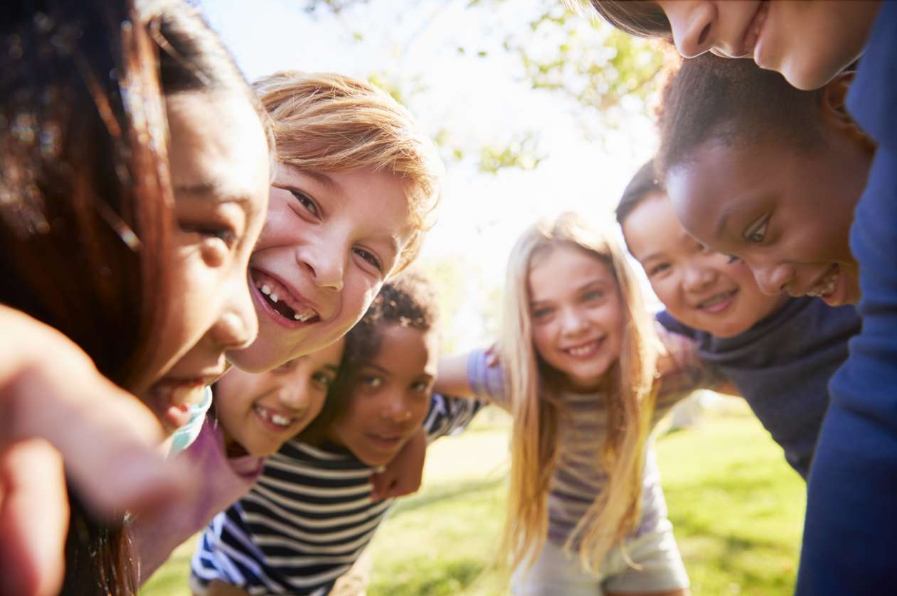 Group of smiling kids stand in a circle with their arms around each other