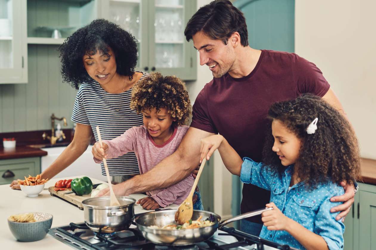 A mother, father, and their two young daughters prepare dinner together.