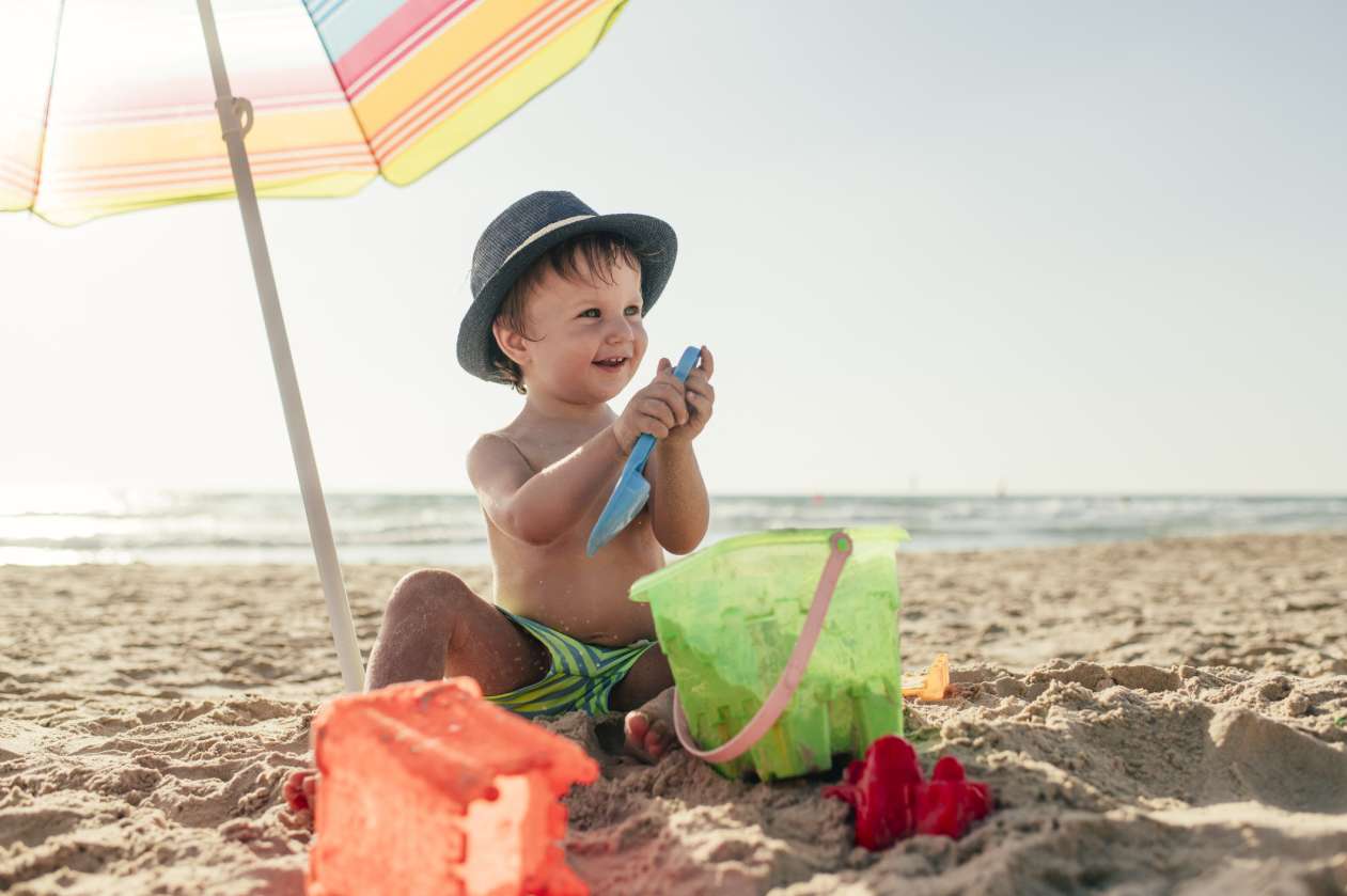 A young boy plays with toys on the beach.