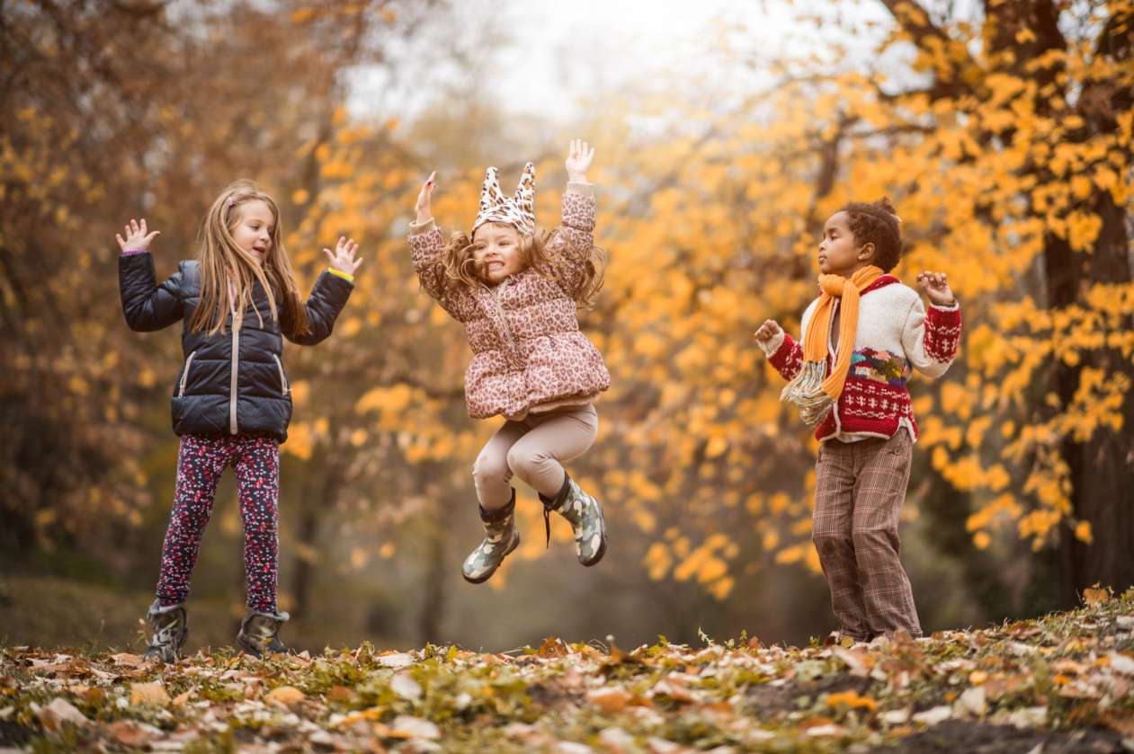 Three girls jump in the air as they play outside on a fall day.