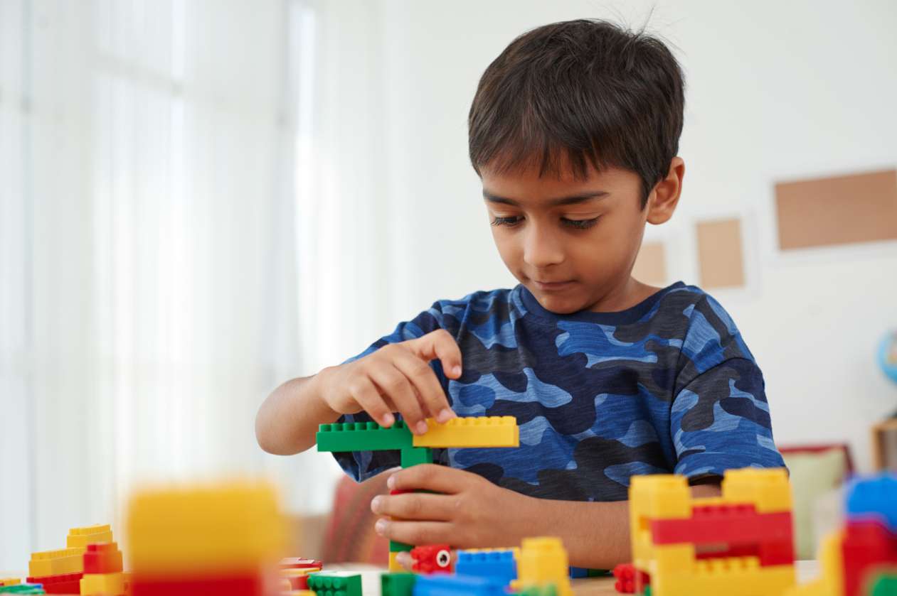 A boy stands in front of a table covered in Lego and starts building a tower.