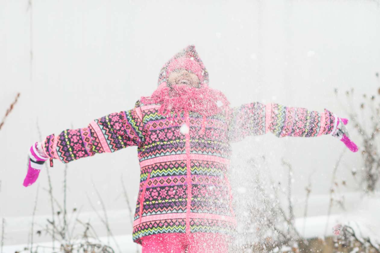 A girl tosses snow over her head and laughs as it falls down around her.