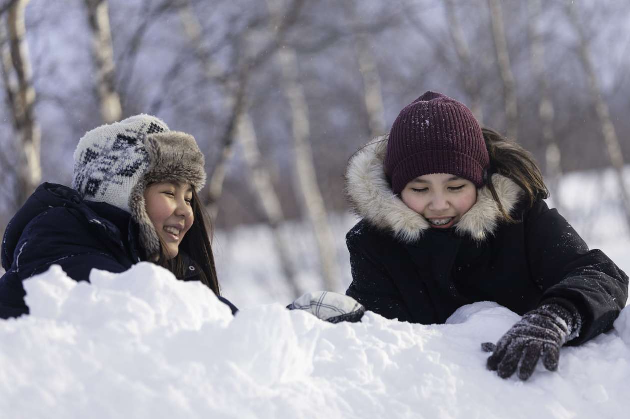 Two tween girls laughing as they sit in the snow