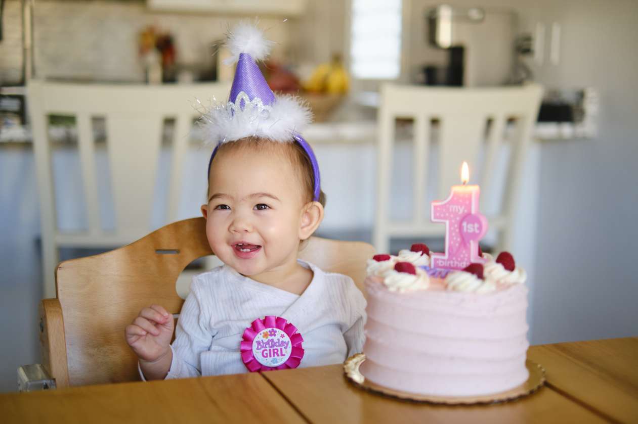 Baby girl sitting at kitchen table in front of birthday cake