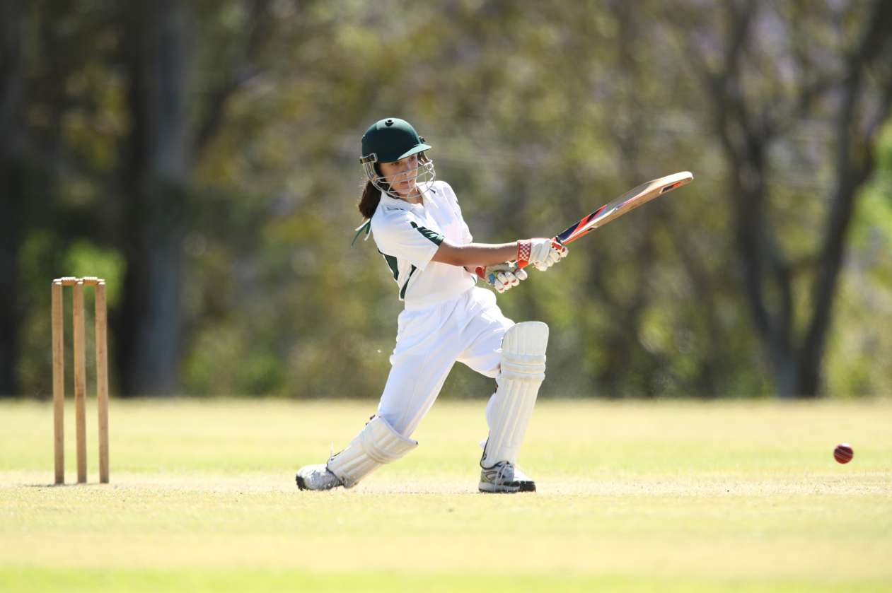 Girl hits cricket ball with bat outdoors on a cricket pitch