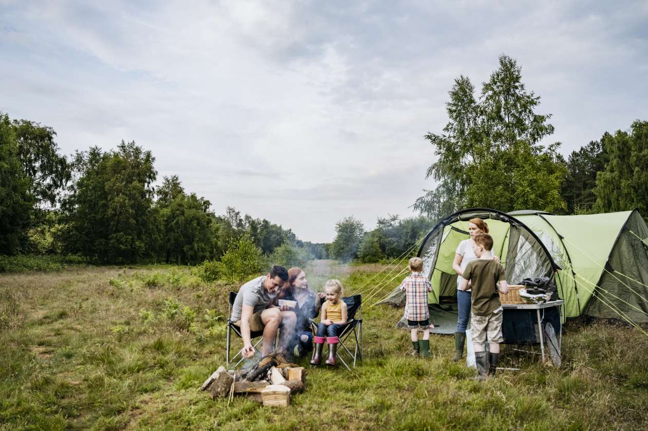 Family sits around a fire, with their tent set up behind them