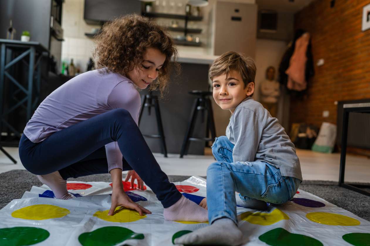 Brother and sister play Twister on the floor in their house.