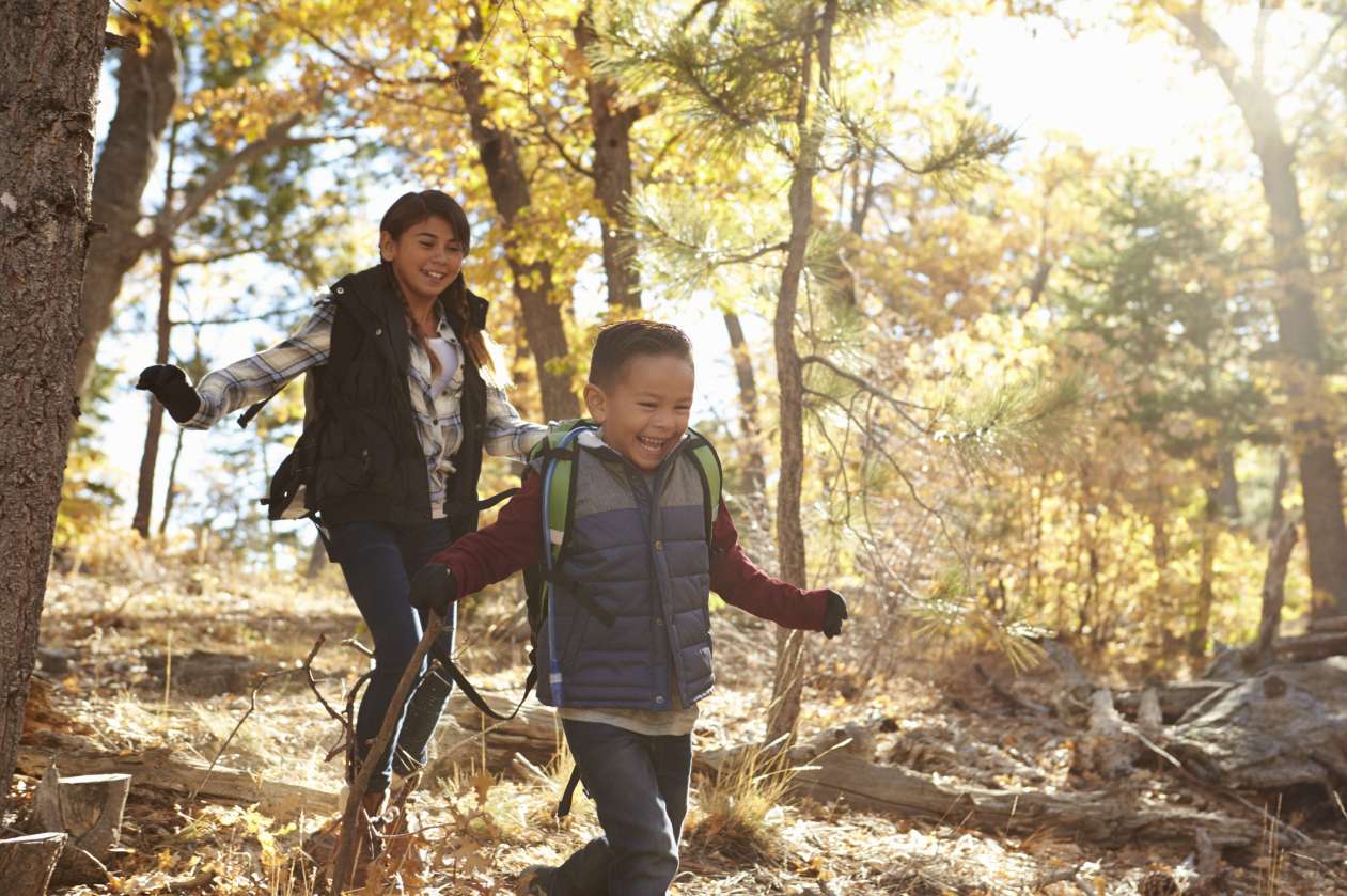 A brother and sister walk in the woods together on a fall scavenger hunt.
