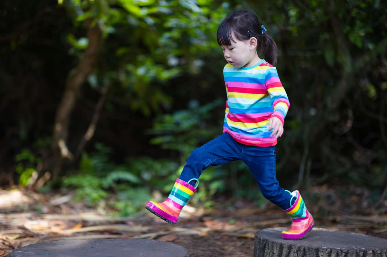 A girl hops from one log platform to another at a nature playground.