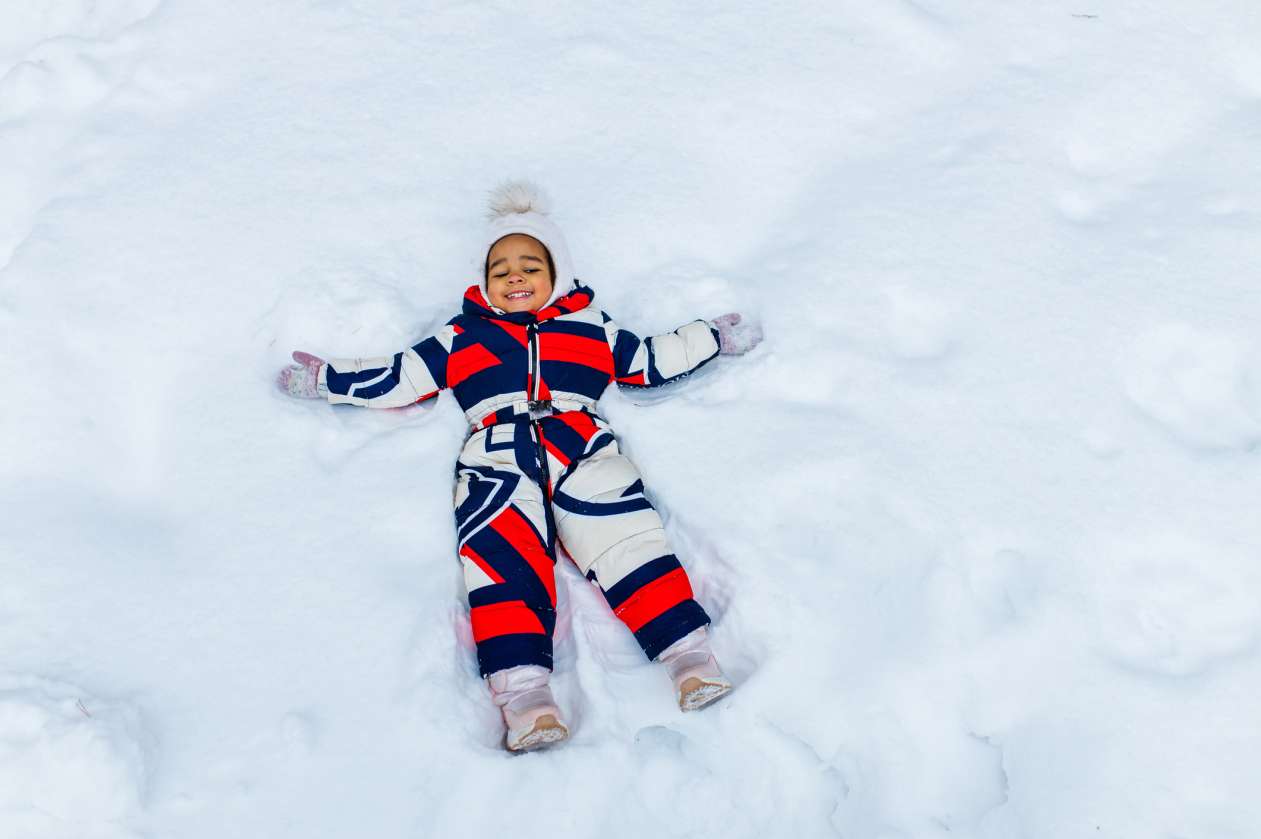 A little girl wearing a snowsuit makes a snow angel.