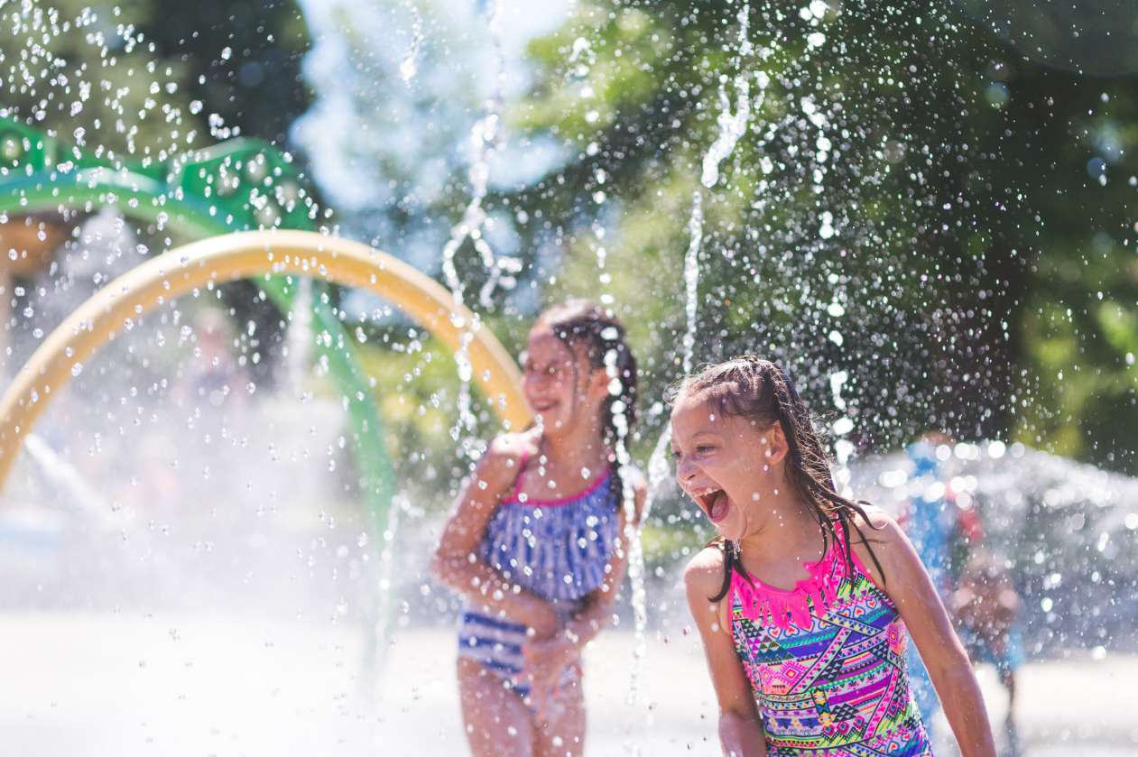 Two girls laugh and scream as they get sprayed with water at a splash park.