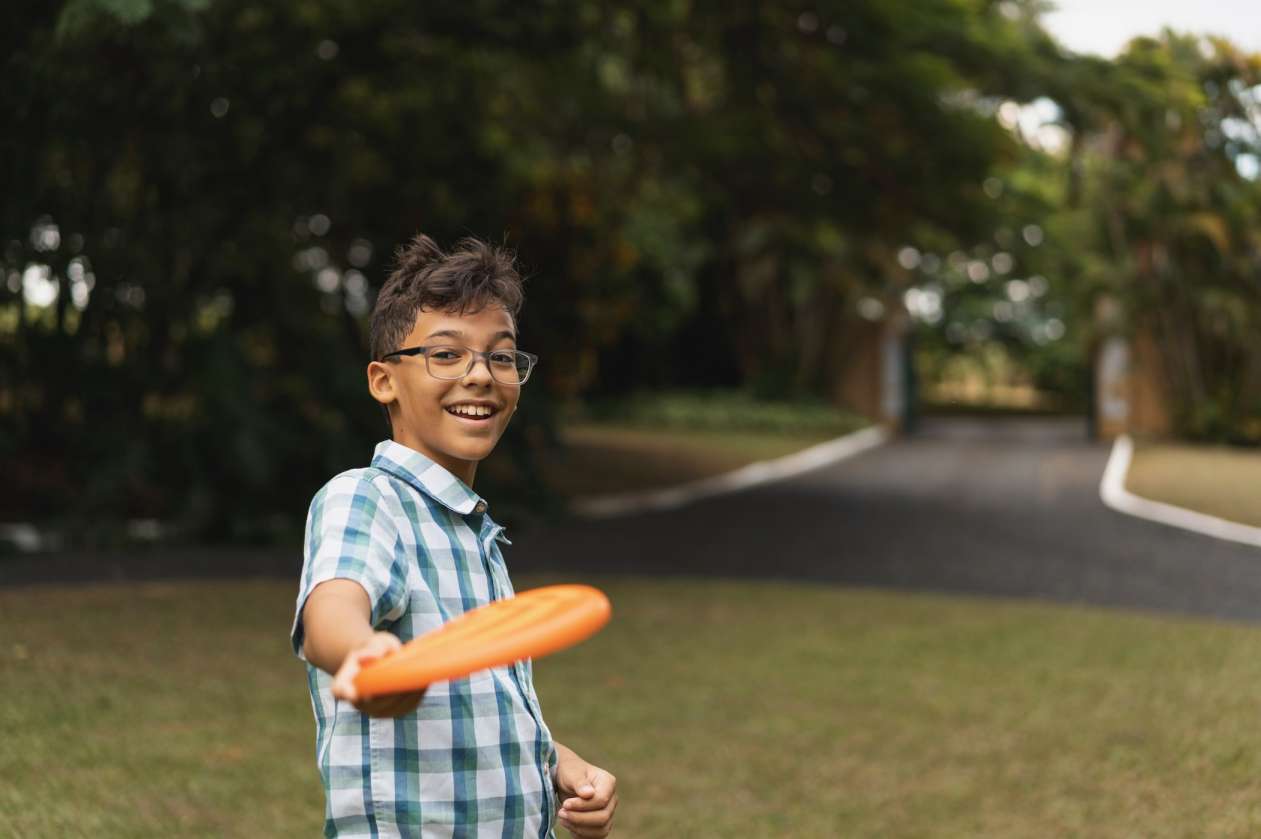 A smiling tween boy throws a frisbee in a park.