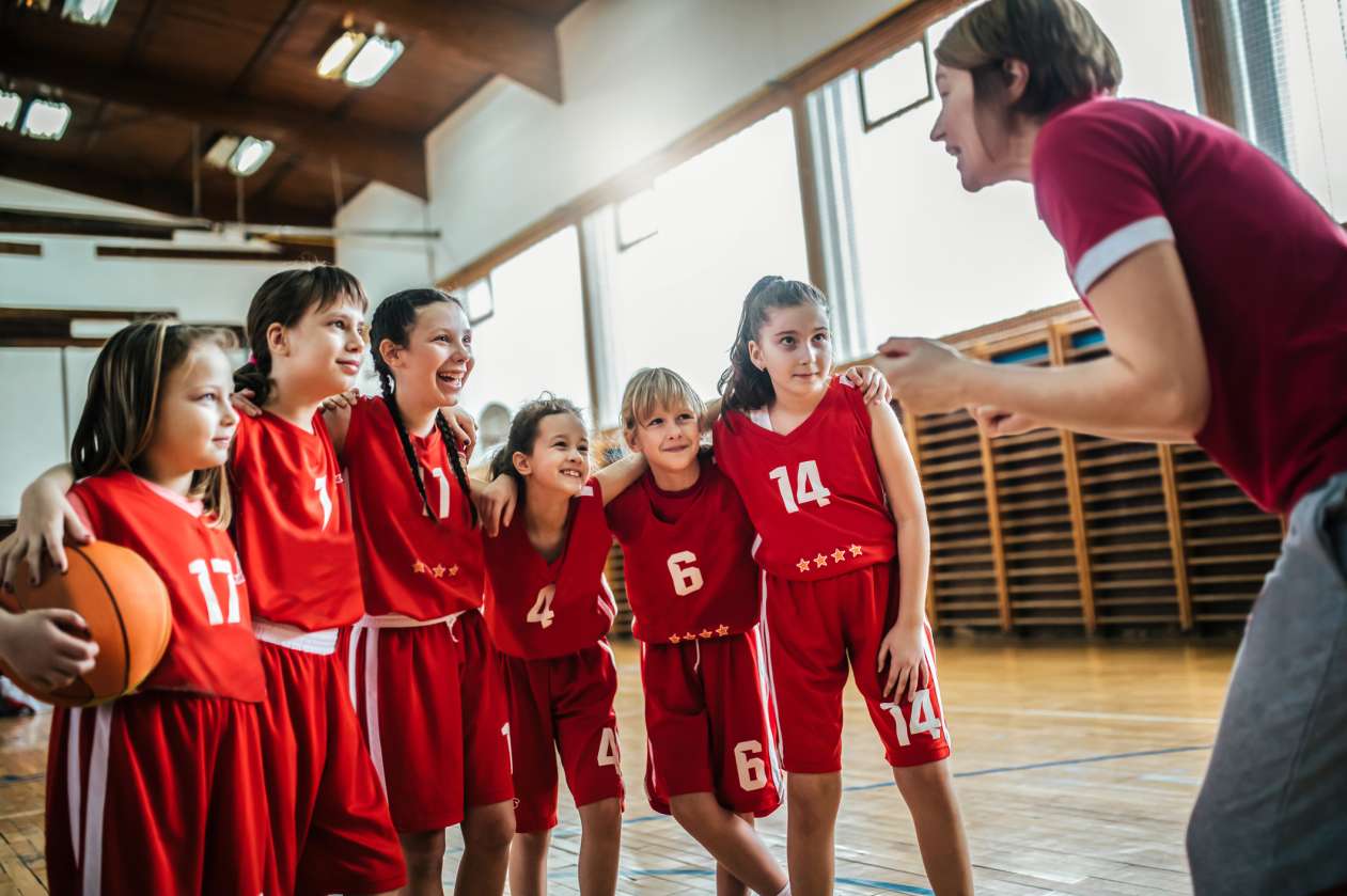 A girls' basketball team stands in front of their coach, who's giving them instructions.