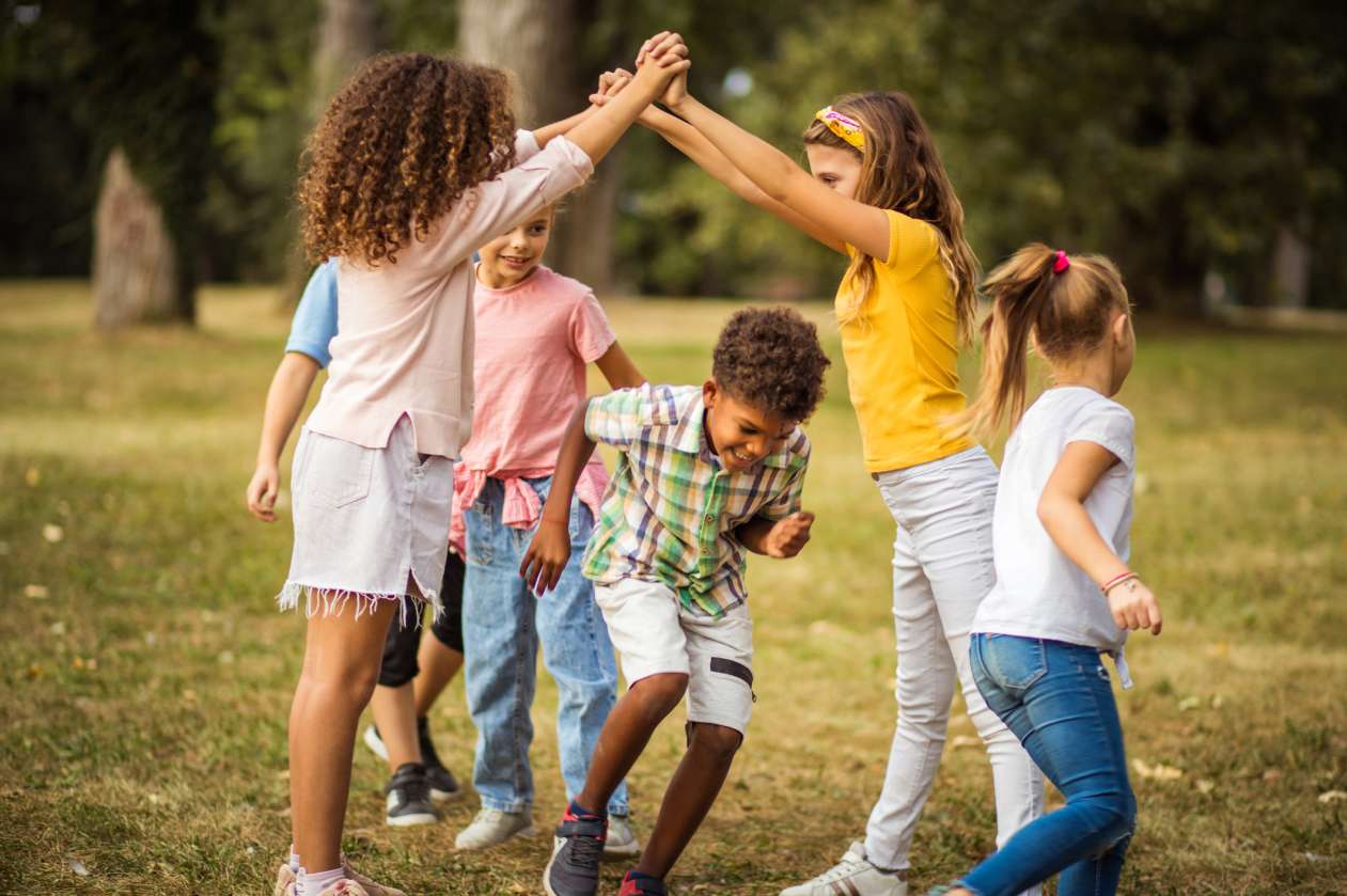 A group of elementary-school-aged kids plays a game together outside on the grass.