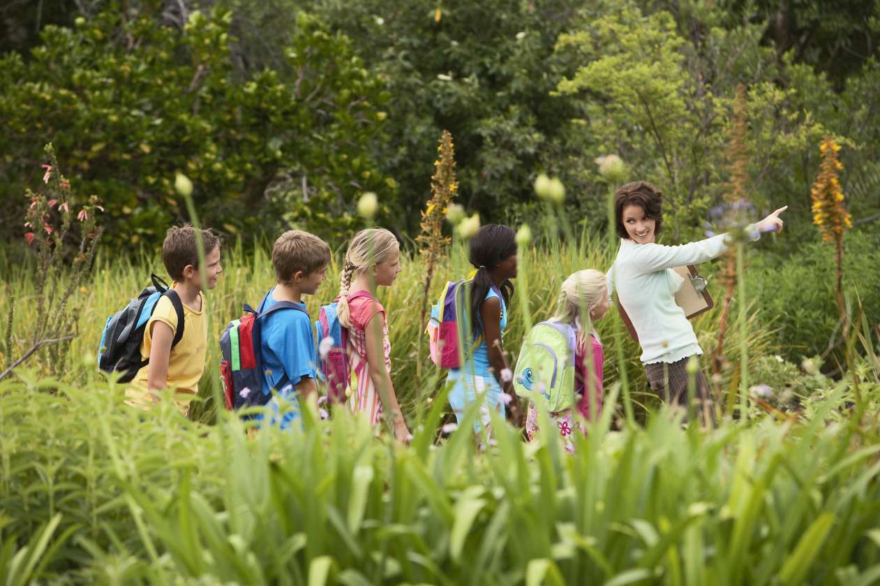 A parent chaperone leads a group of students through a nature area.