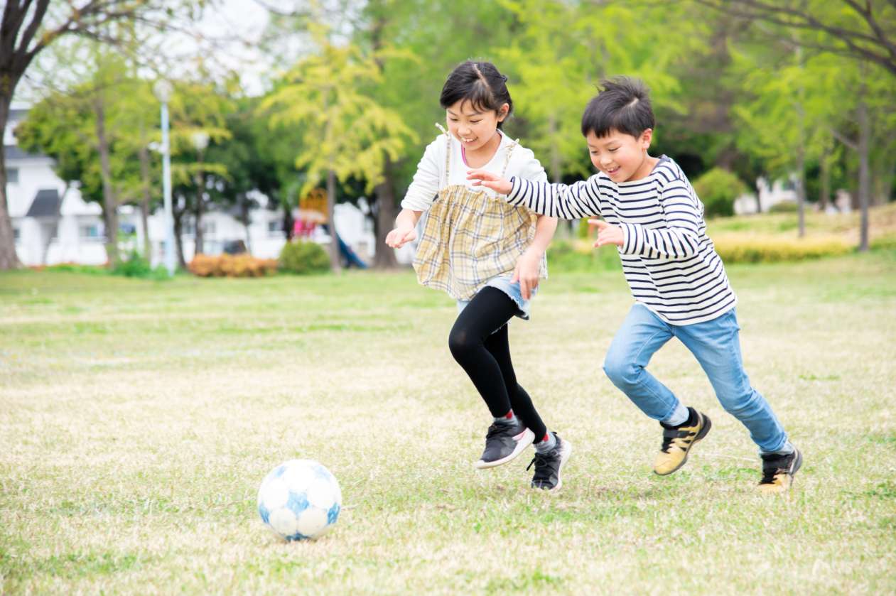 A boy and a girl chase a soccer ball in a park.