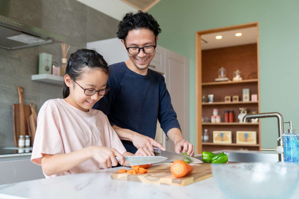 A father and his preteen daughter chop vegetables together at the kitchen counter.