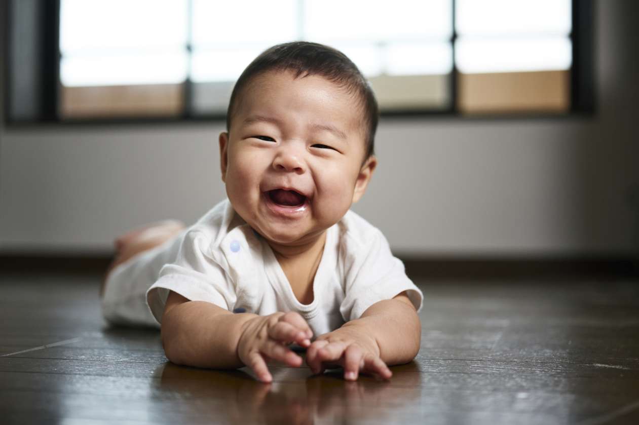 A baby lies on his stomach on the floor, smiling. 