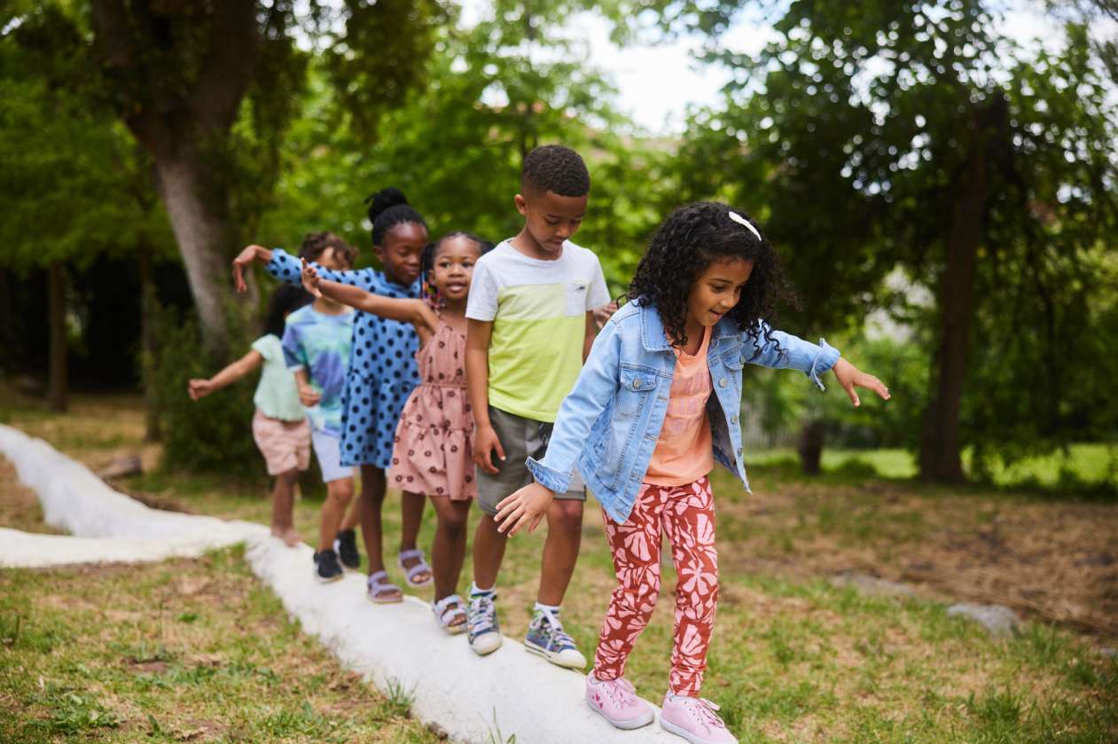 A group of children balance carefully as they walk across a log in single file.