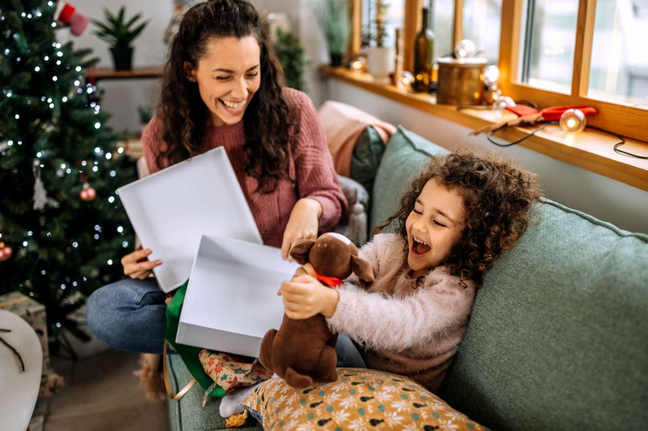 A mother and her young daughter open presents on the couch on Christmas morning.