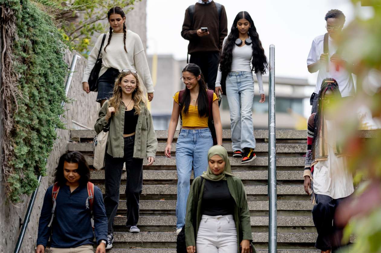 A group of teenagers walks down an outdoor set of stairs at a high school or university.