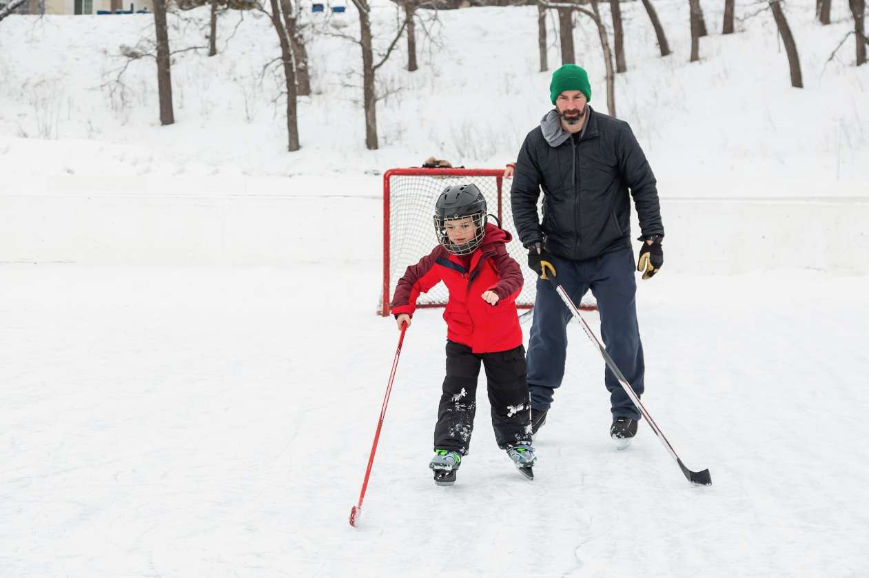 A young boy and his dad play hockey together on an outdoor rink.