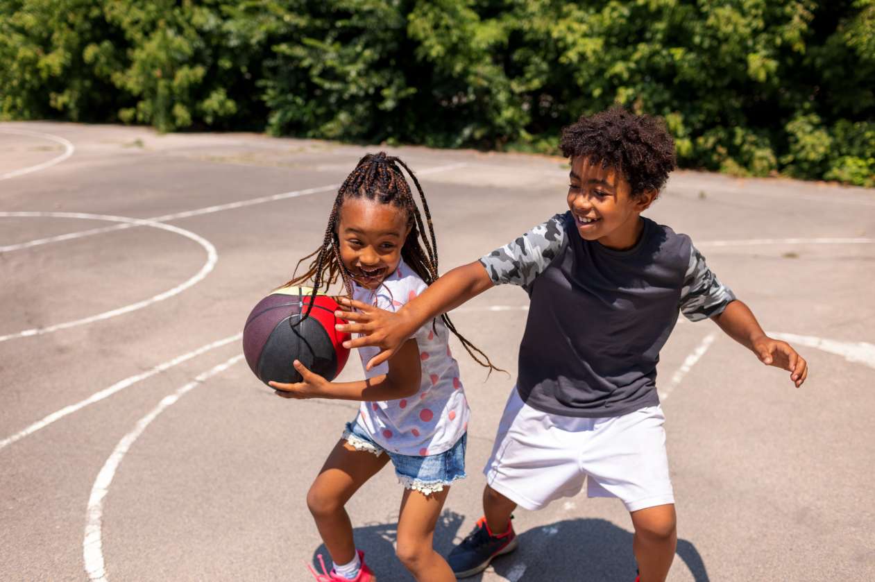 A boy and a girl play basketball on an outdoor court.