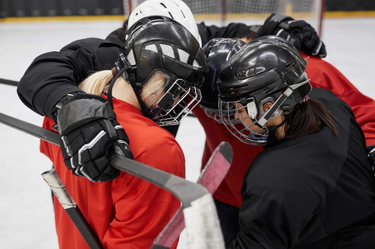 A group of female hockey players huddle on the ice.